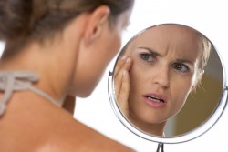 Concerned young woman looking in mirror